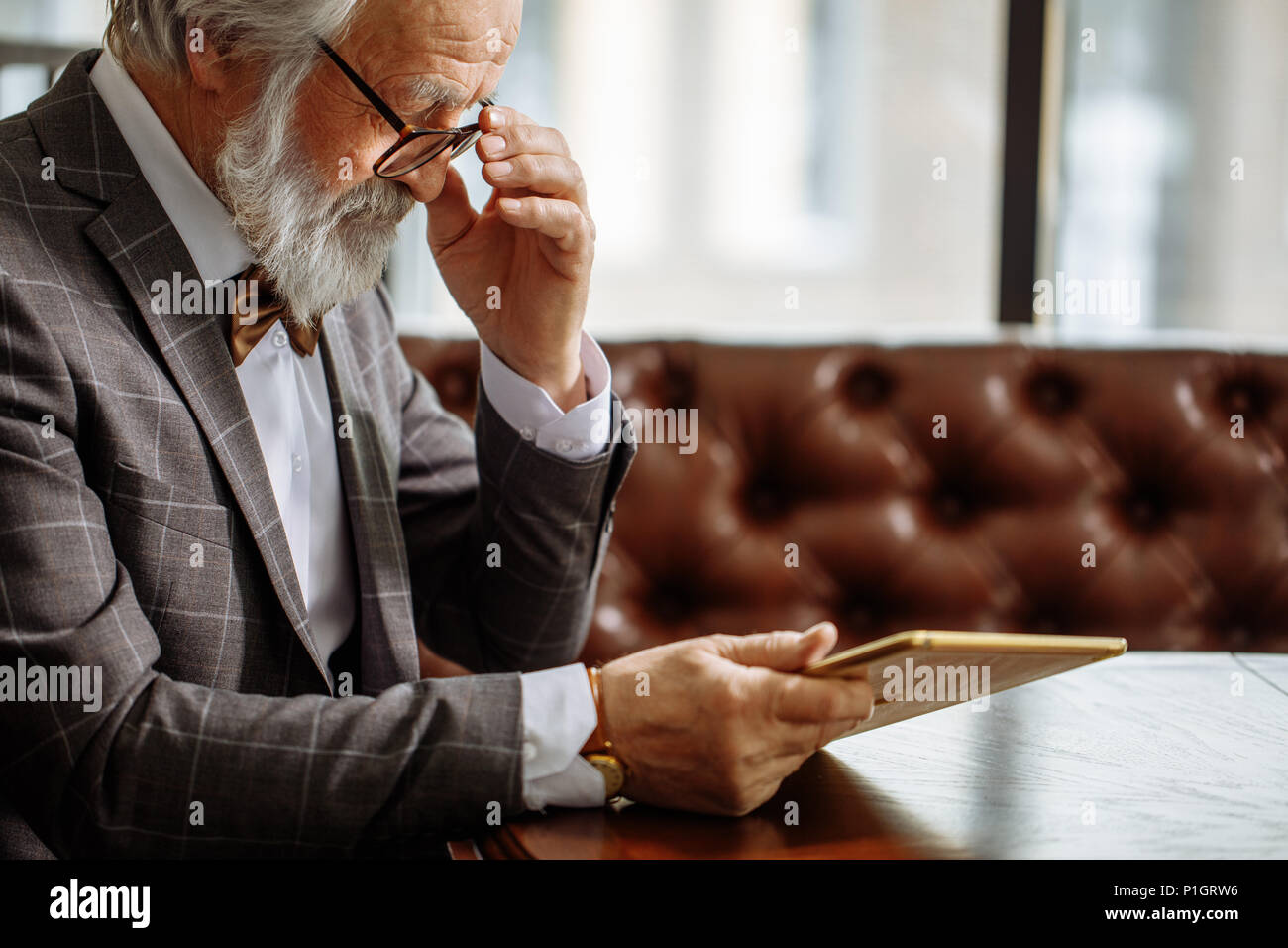 grey haired man in glasses using iPad at home Stock Photo