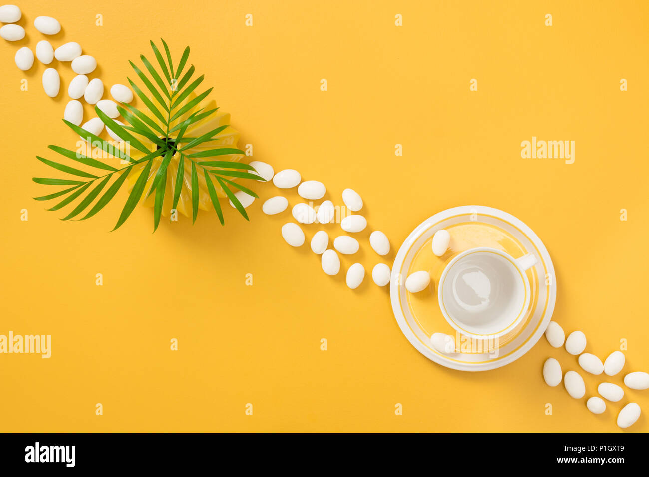 White chocolate candies, palm tree leaves and teacup on yellow background. Stock Photo