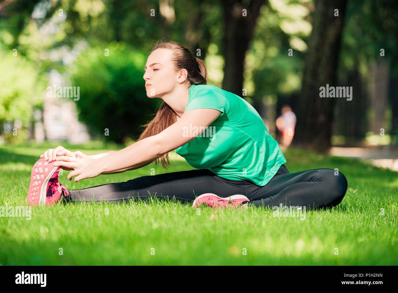 Young pretty woman sitting on the grass and stretching her legs Stock ...