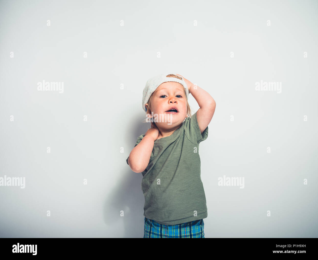 A cute little toddler boy wearing a baseball cap is striking a pose on a white background Stock Photo