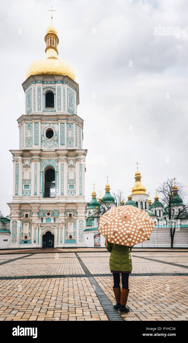 Young woman stands under umbrella in square and in front of Bell tower of St. Sophia Cathedral, Kiev, Ukraine Stock Photo