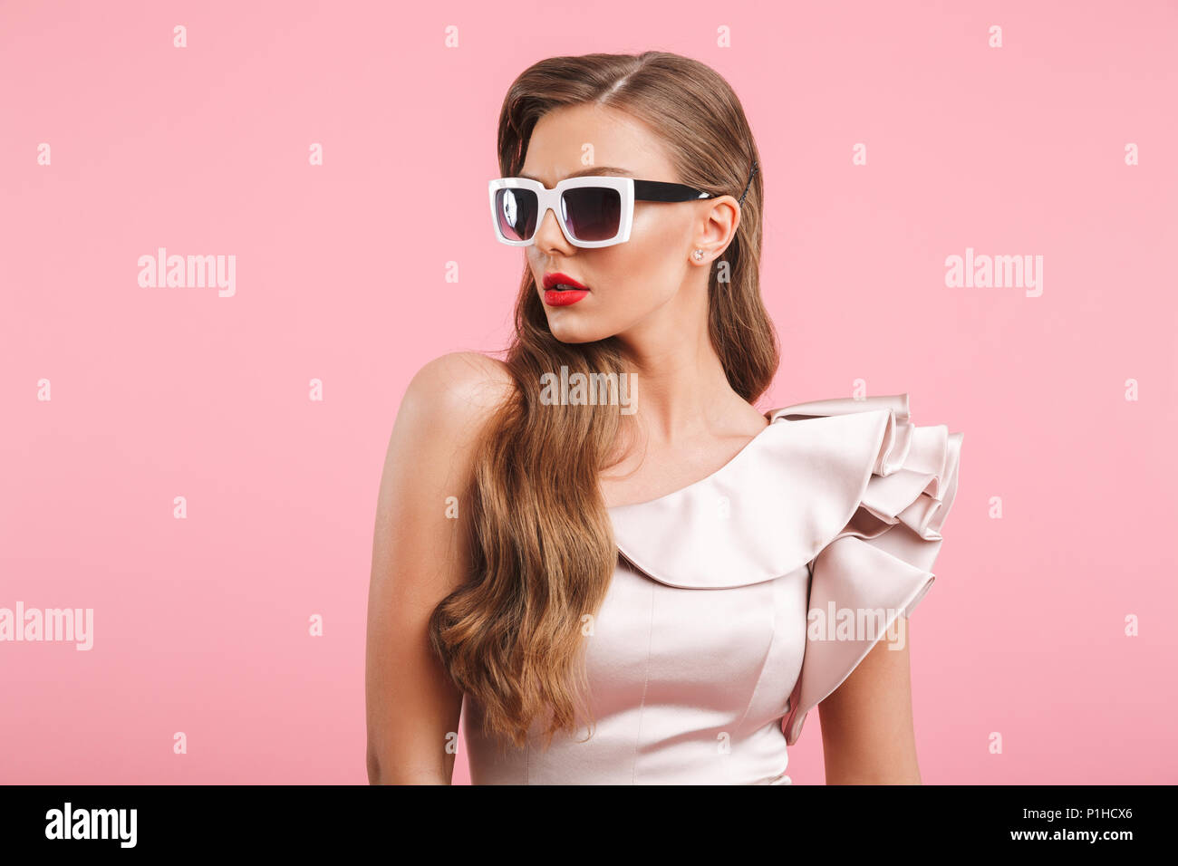 Portrait closeup of fashionable woman 20s in dress looking aside in stylish square sunglasses isolated over pink background Stock Photo