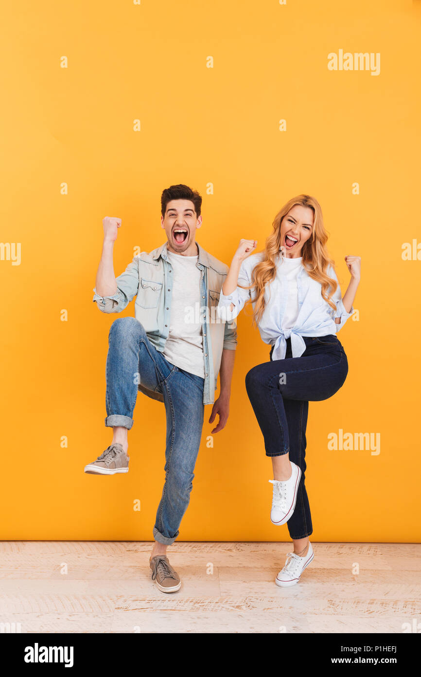 Full length photo of joyful young couple rejoicing and clenching fists like winners isolated over yellow background Stock Photo
