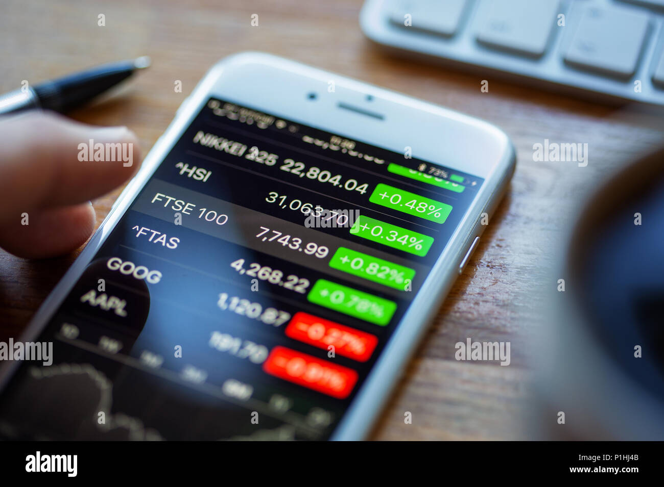 BATH, UK - JUNE 11, 2018 : An Apple iPhone 6 on a desk displaying stock market information using the Apple Stock app. A human hand hovers above the FT Stock Photo