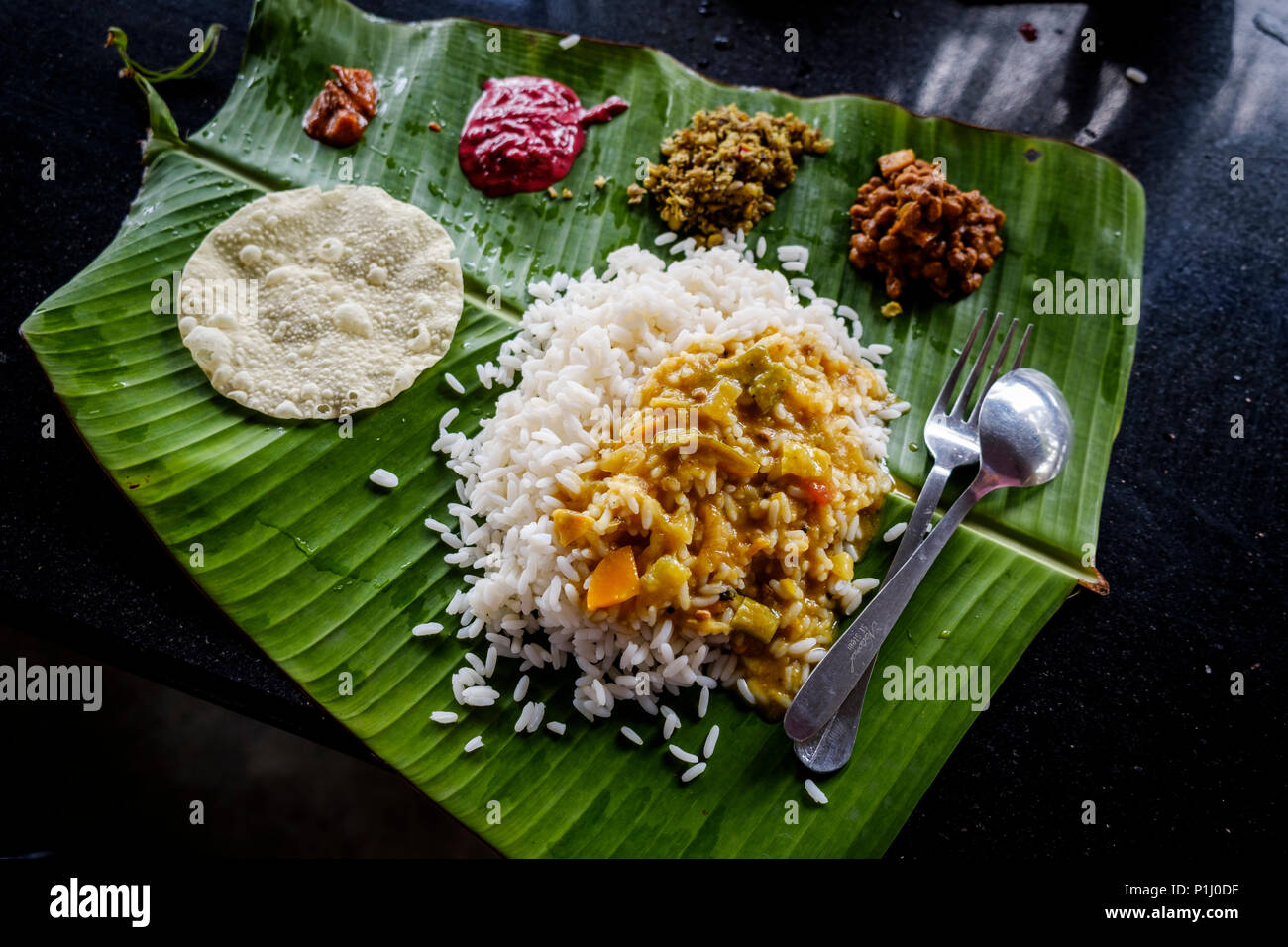 Sadya, the Kerala version of 'thali', a typical South India meal of rice, sambar (lentil stew), chutneys and pickles served on a banana leaf. Stock Photo