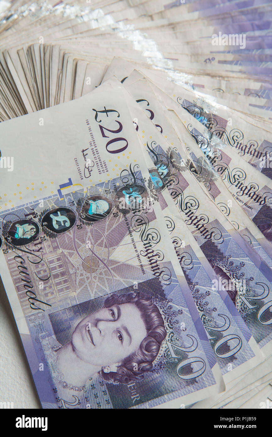 A pile of British twenty pound notes on a white paper background Stock Photo