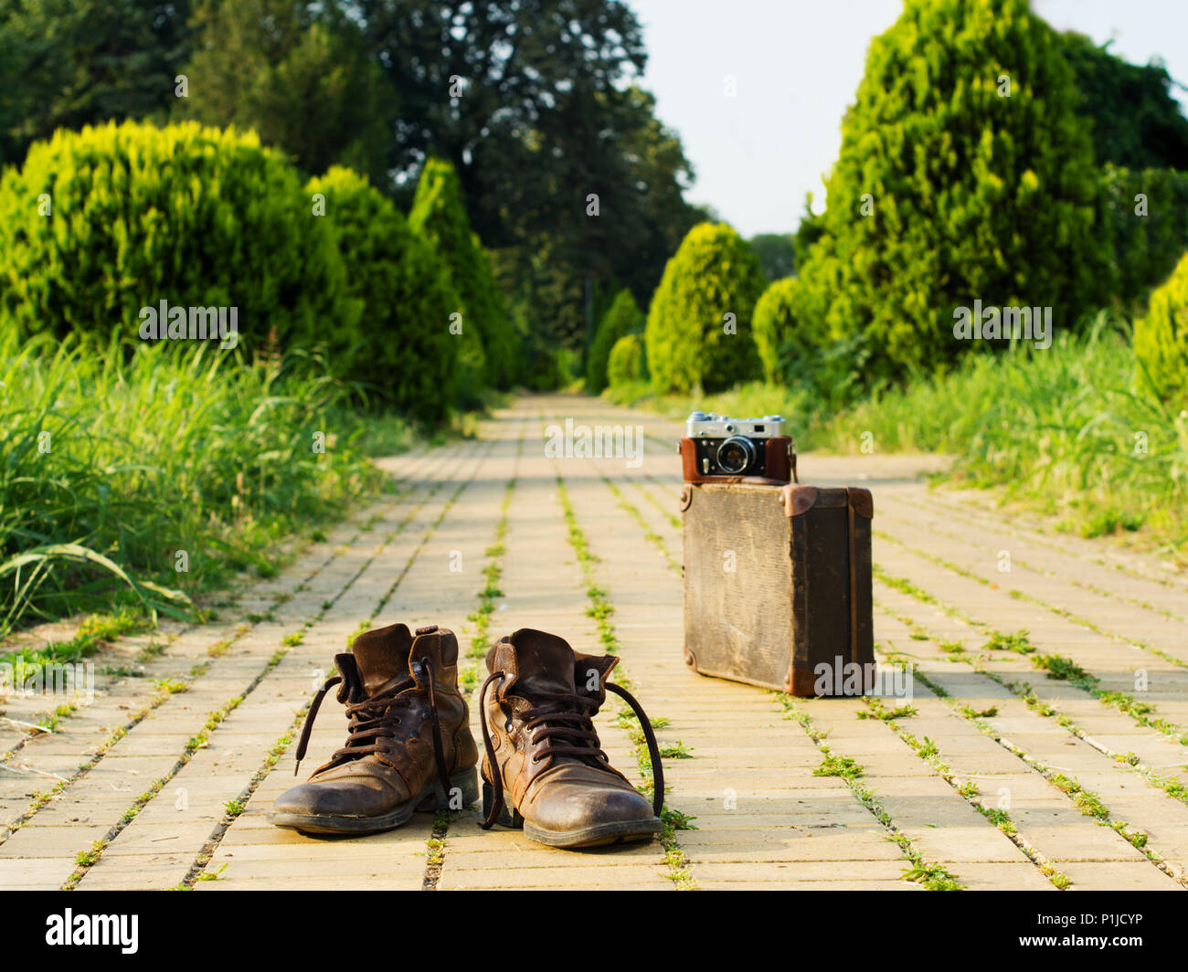 It’s time to wander the world and collect memories. Shabby boots in a foreground. An analog camera on a vintage suitcase, in a blurry background. Stock Photo