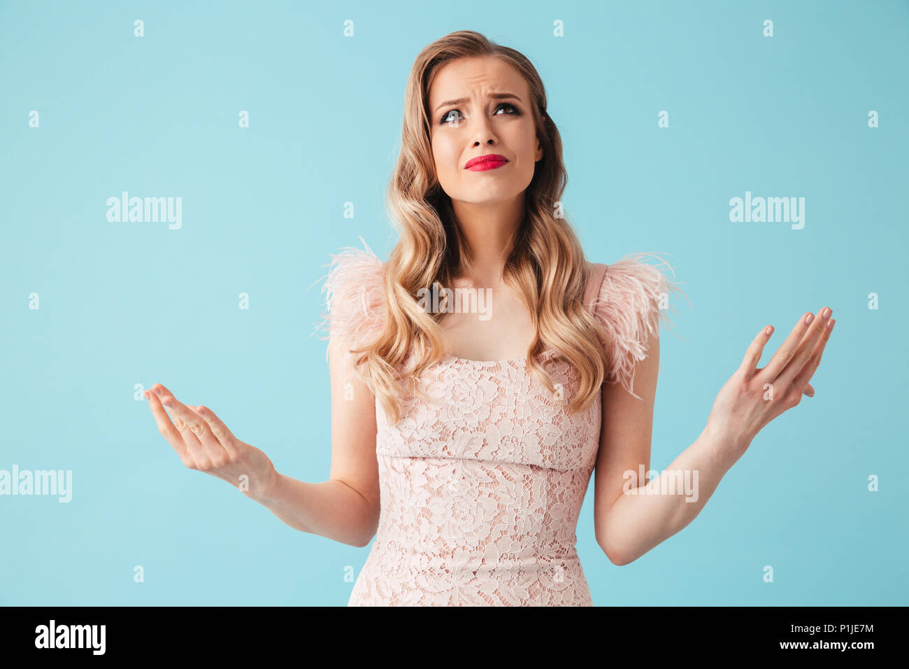Image of Confused displeased blonde woman in dress looking up over turquoise background Stock Photo