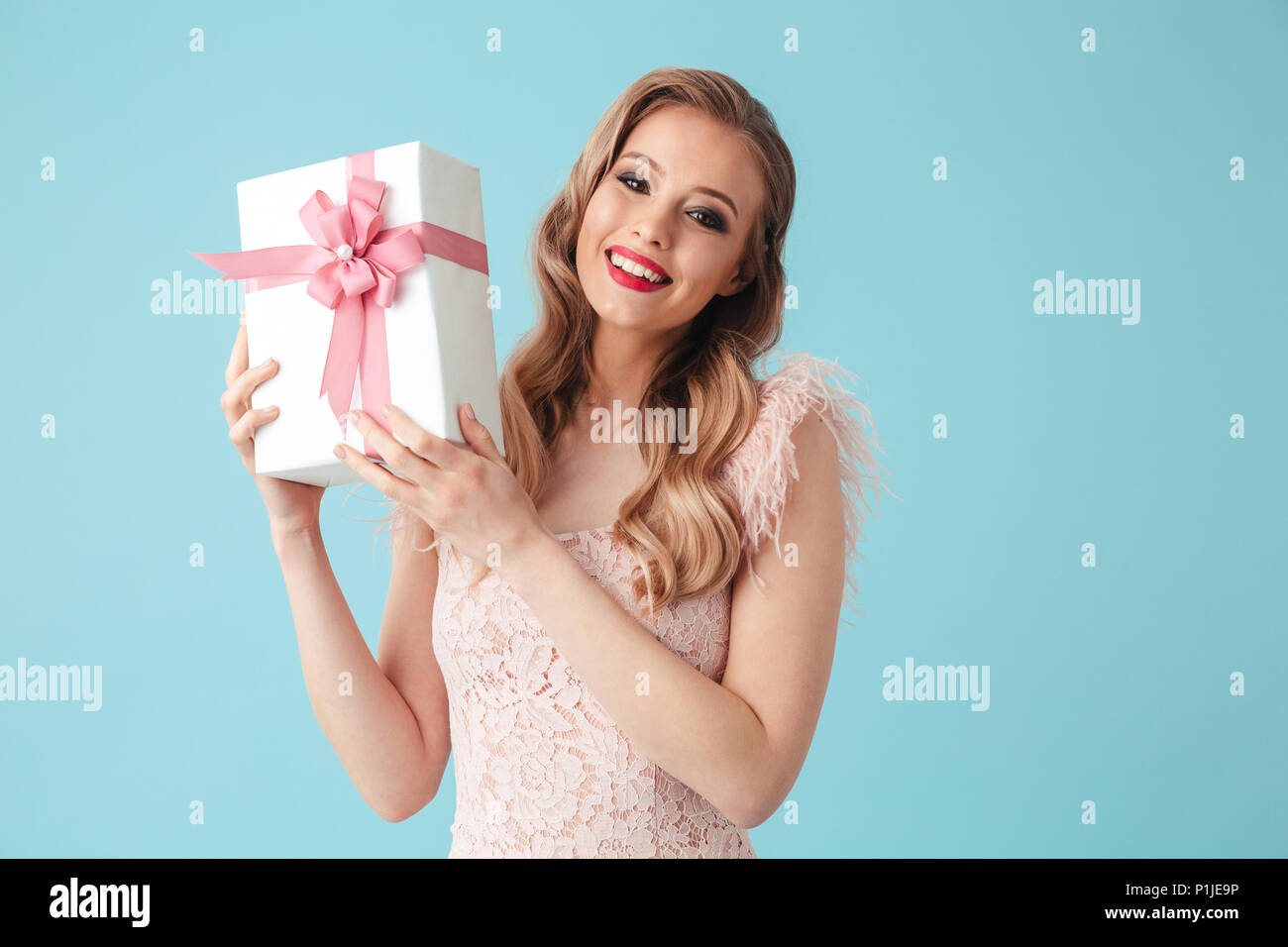 Smiling blonde woman in dress holding gift box and looking at the camera ovr turquoise background Stock Photo