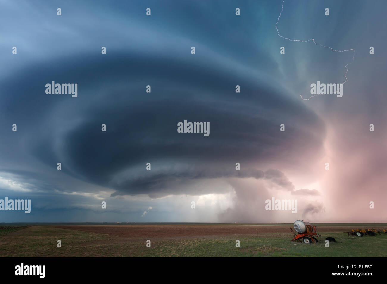 Supercell with cloud-to-cloud and sheet lightning above a field with agricultural machines near Vega, Oldham County, Texas, USA Stock Photo