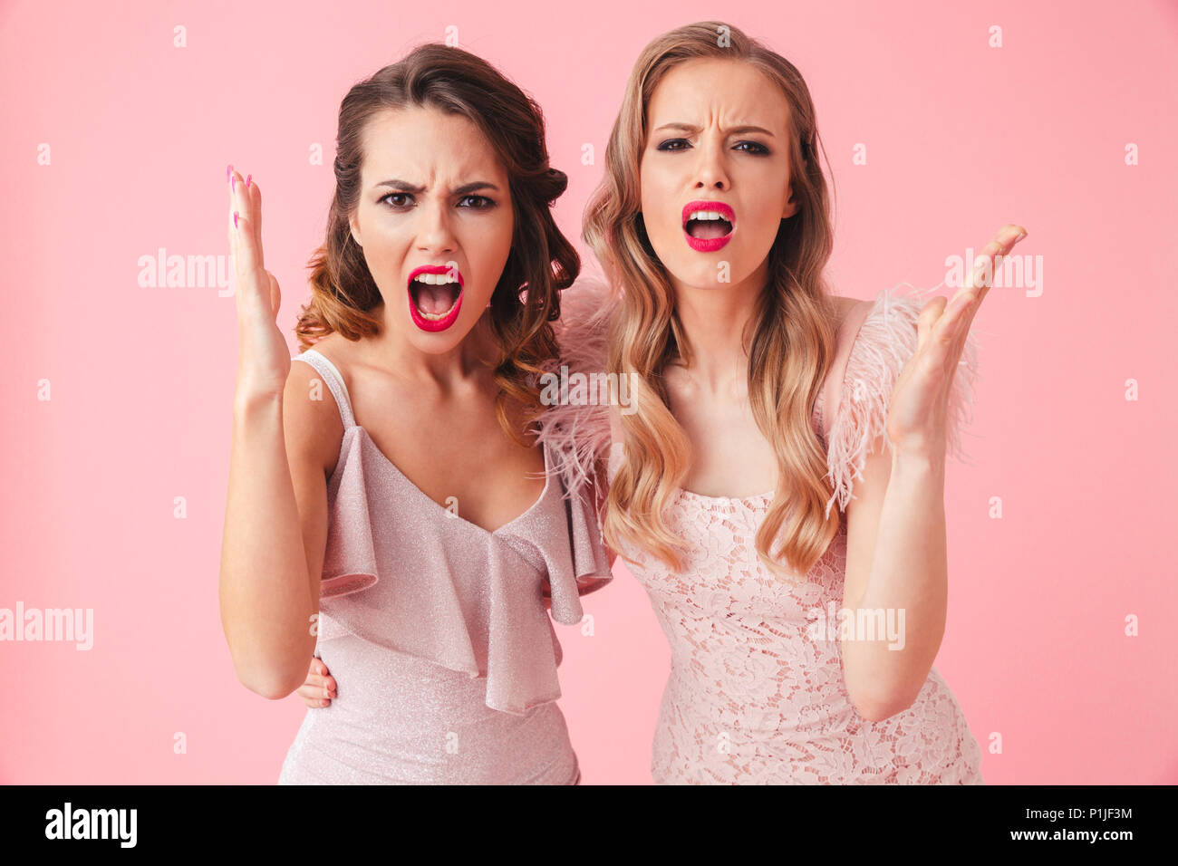 Two displeased angry women in dresses screaming and looking at the camera over pink background Stock Photo