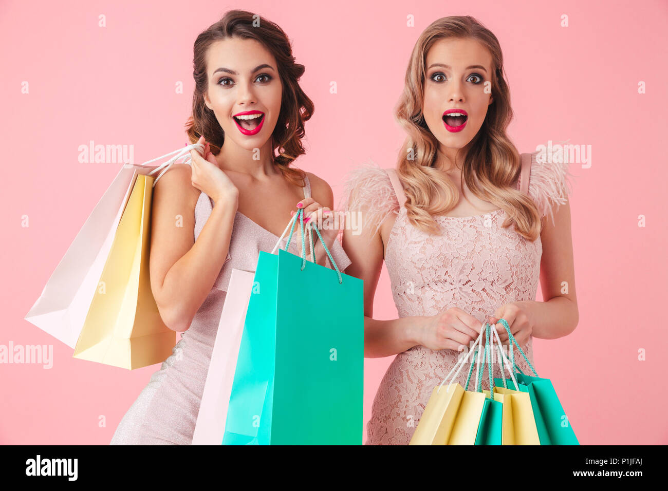 Two Happy elegant women in dresses holding packages and looking at the camera over pink background Stock Photo