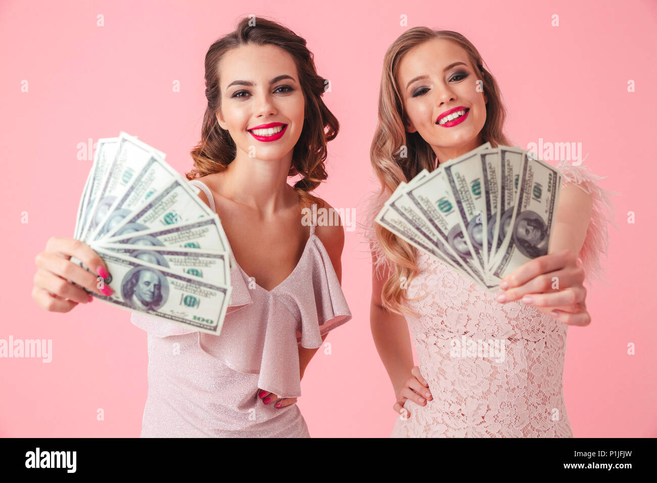 Two young gorgeous women 20s in dresses showing fan of money 100 dollar ...