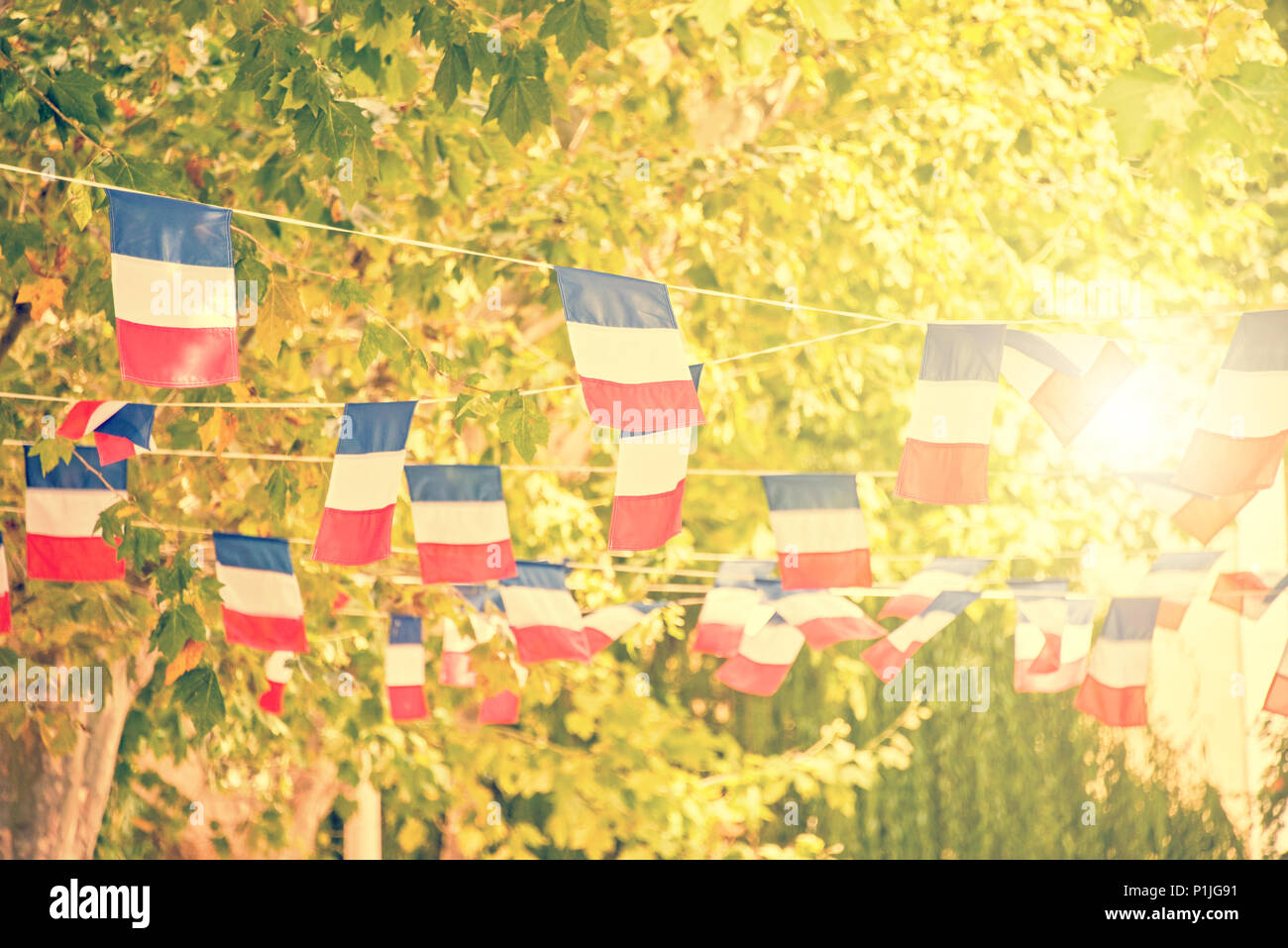 French flags garland, plane trees and sun background in a village square Stock Photo