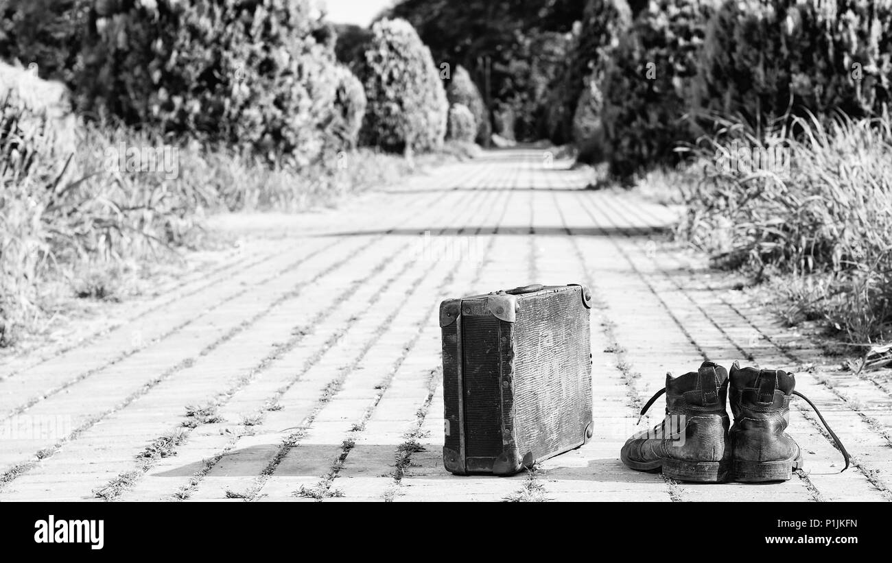 Wanderlust! Old leather ankle boots and an antique cardboard suitcase with metal reinforcements at the corner, in the middle of a brick road. Stock Photo
