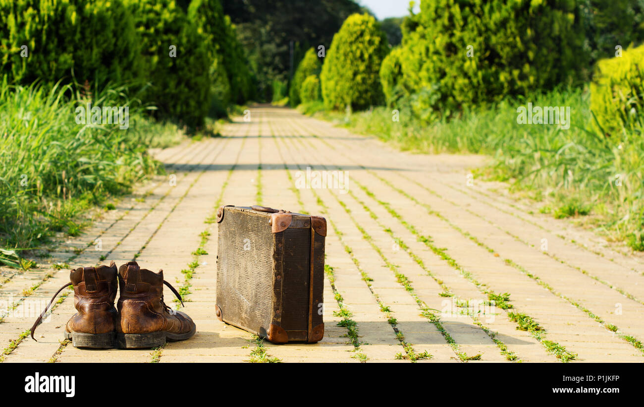 It’s time to wander the earth! Shabby ankle boots and a vintage suitcase in the middle of a yellow brick road. Sixteen-by-Nine crop. Stock Photo