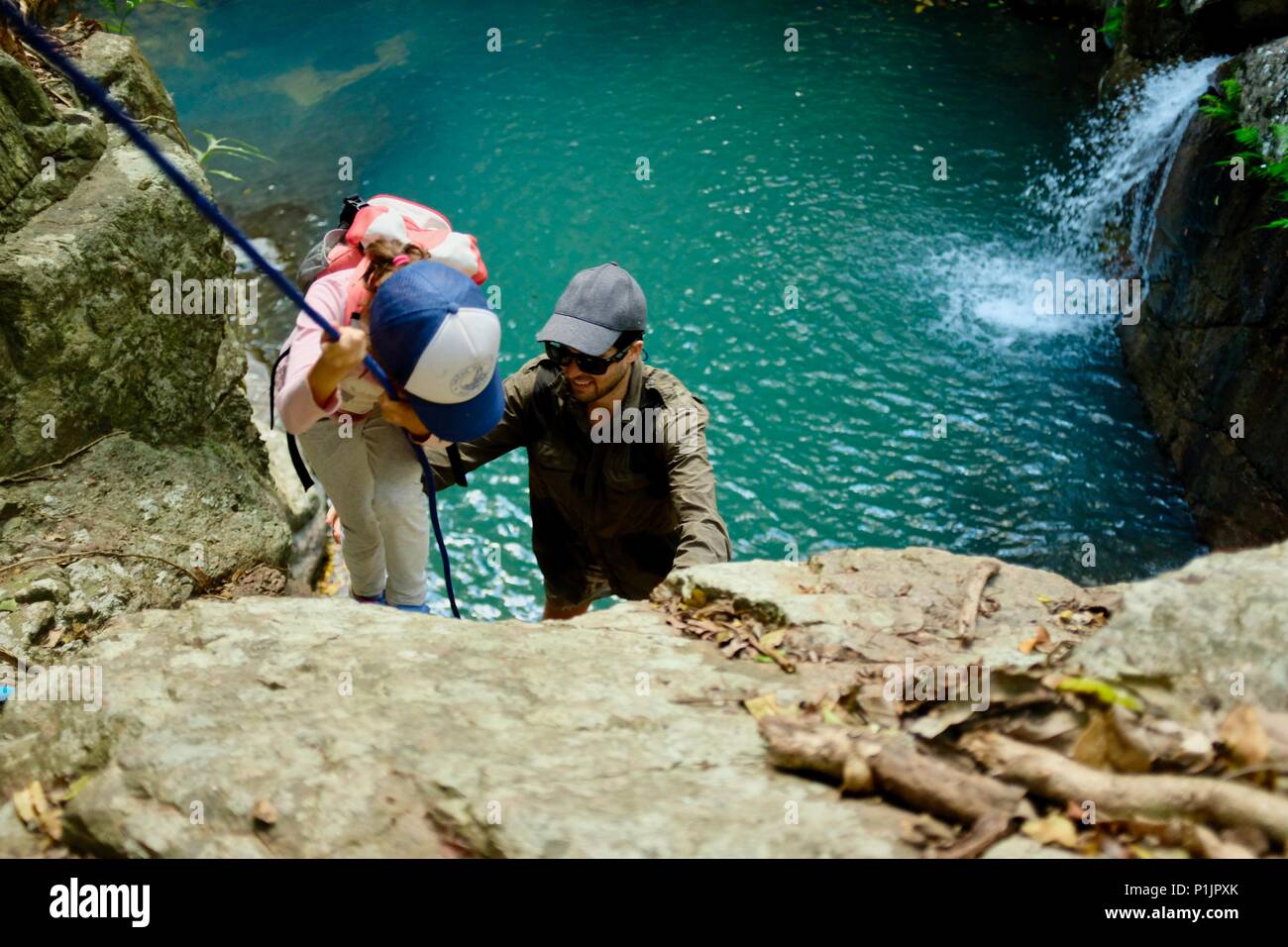 Father helps child to climb down rope at the tranquil blue waters of