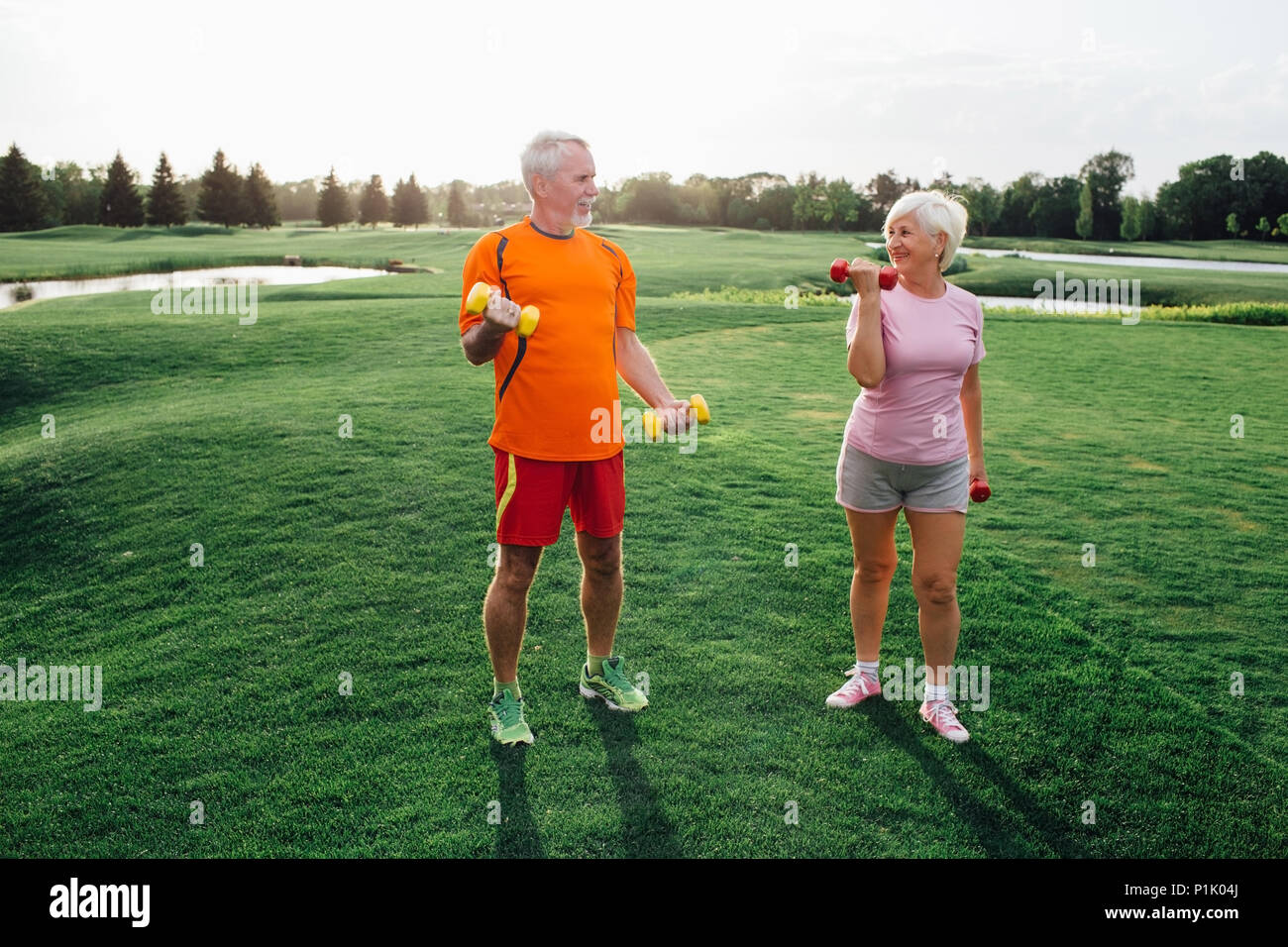 senior man and woman practice fitness exercise with dumbbells in a park at sunny day Stock Photo