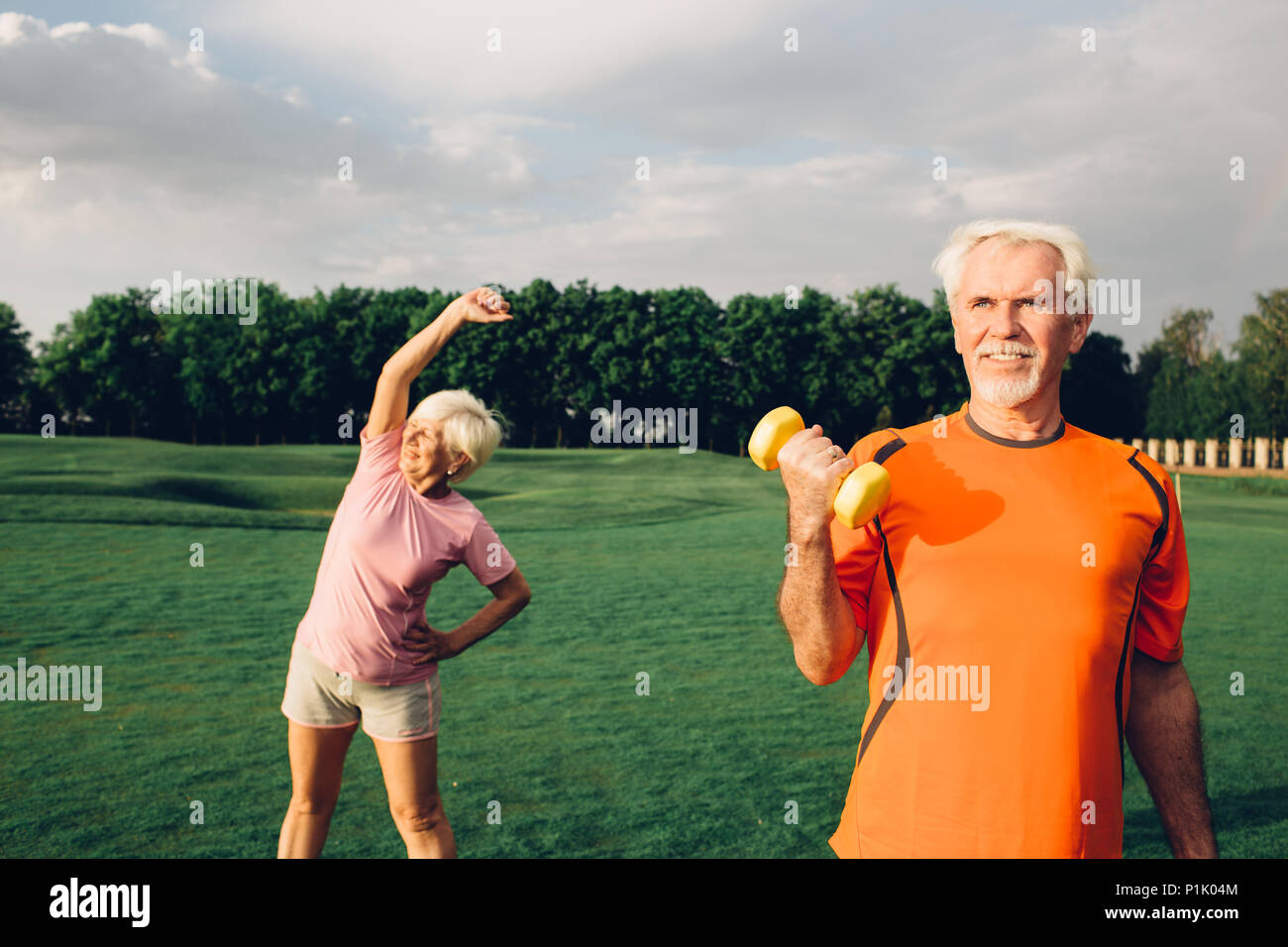 senior man and woman working out with dumbbells in a park at sunny day, focus on man Stock Photo