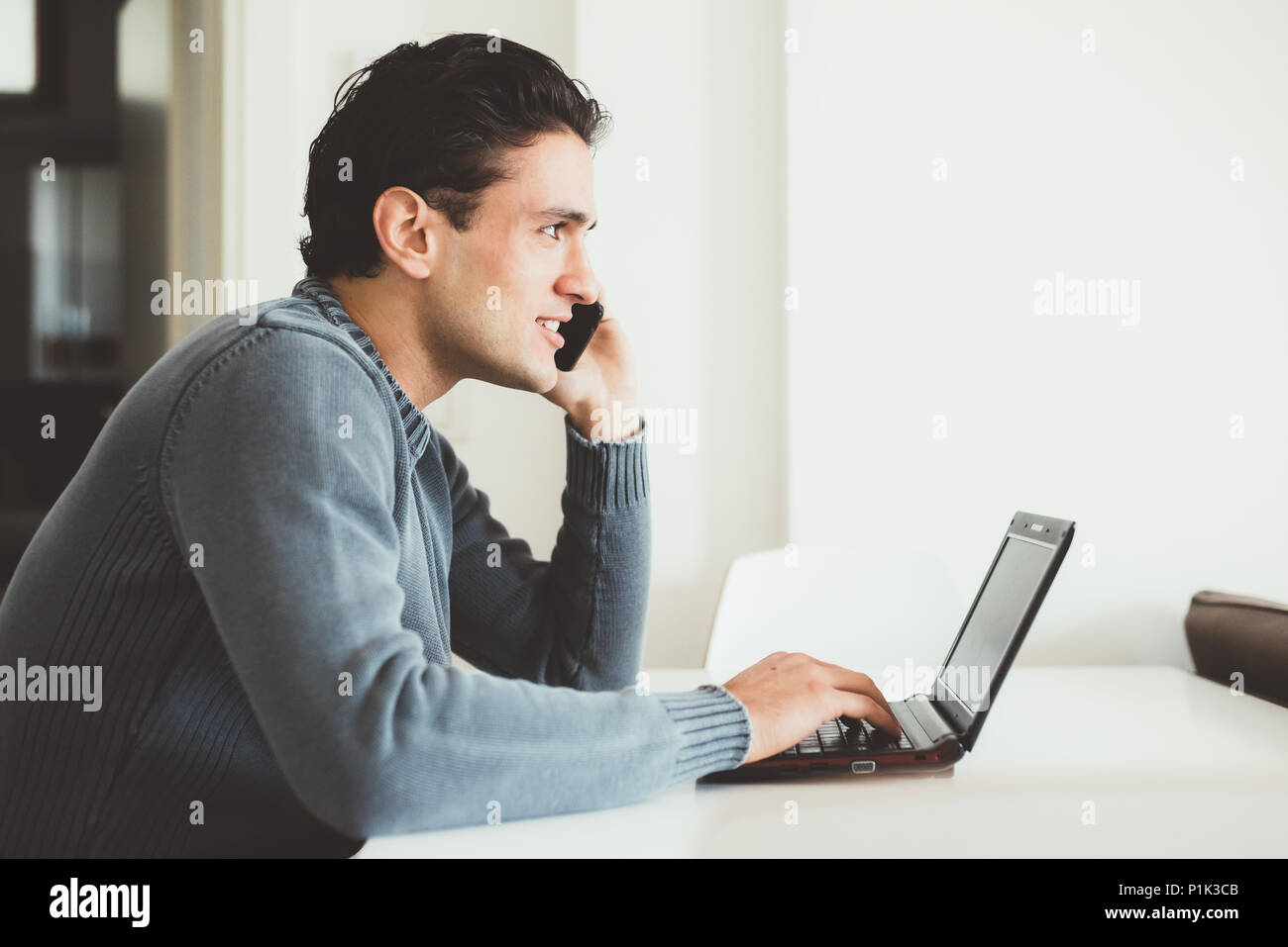 Handsome young man sitting indoor talking smart phone using computer - business, technology, internet concept Stock Photo