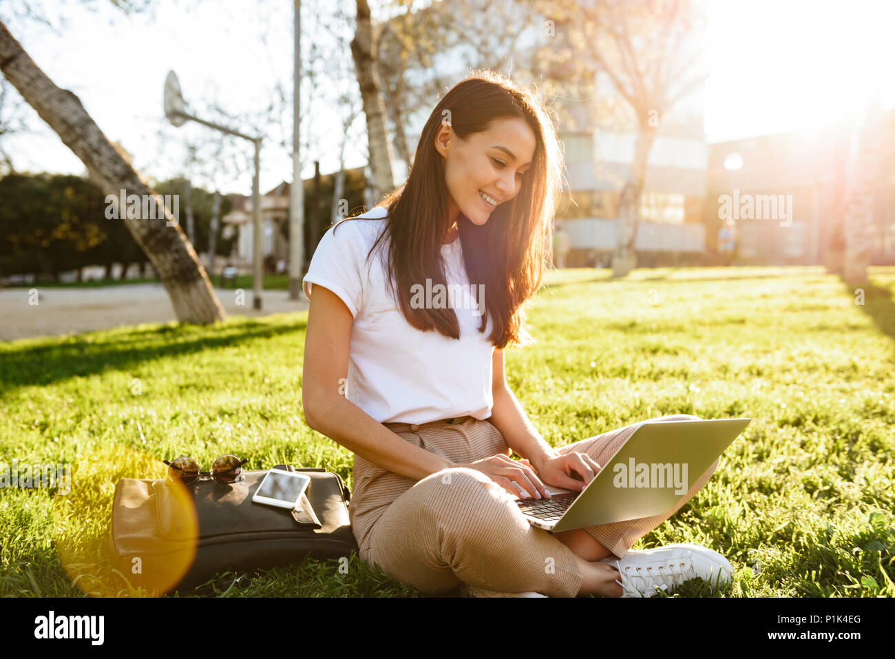 Image of gorgeous beautiful woman sitting on grass outdoors using ...
