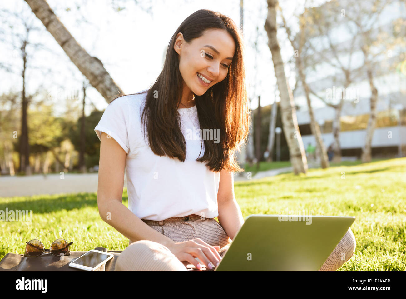Image of gorgeous beautiful woman sitting on grass outdoors using ...