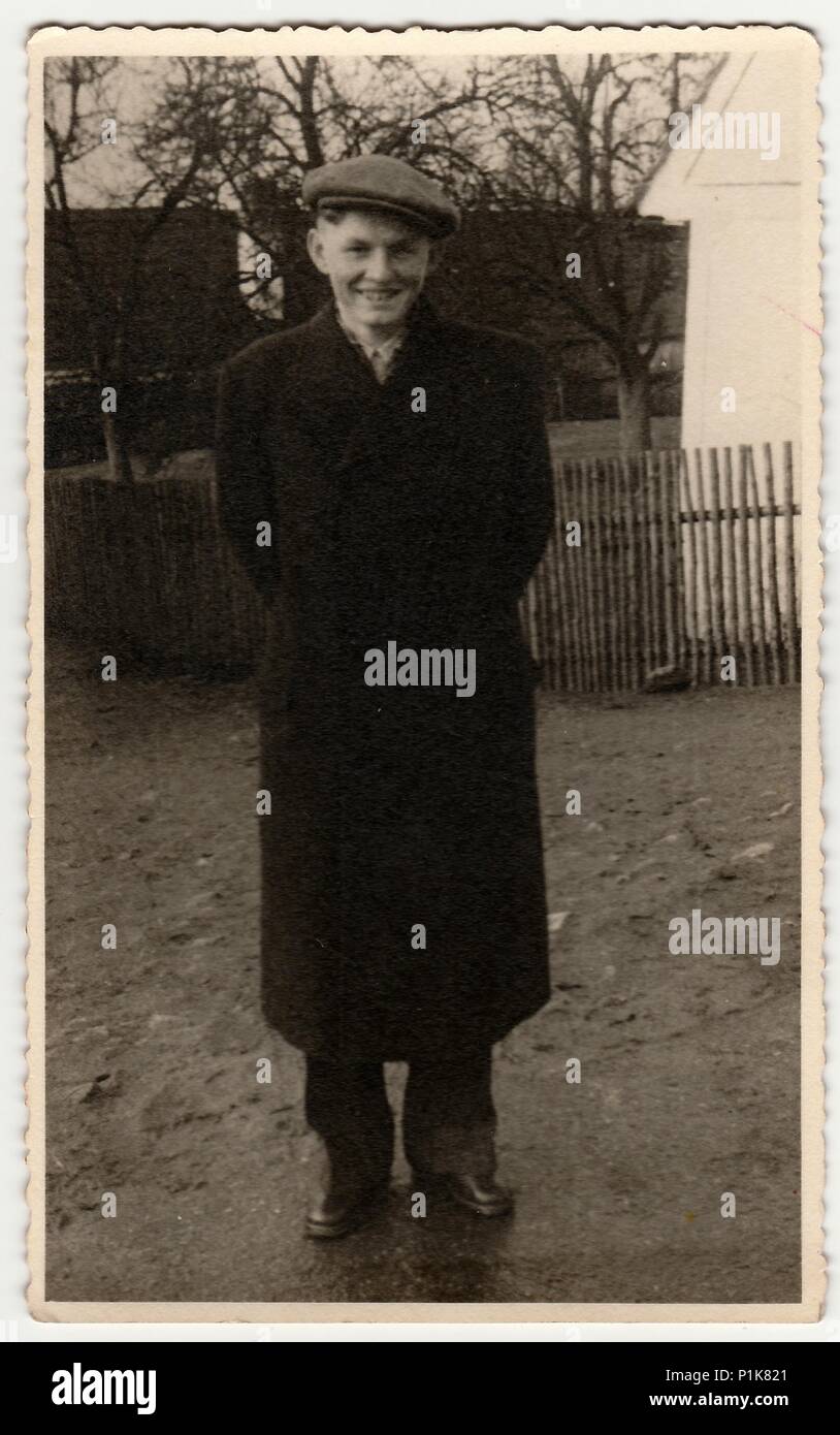 THE CZECHOSLOVAK SOCIALIST REPUBLIC - CIRCA 1950s: Vintage photo shows young man wears peaked cap, poses outdoors. Wooden fence and house is on background.  Black & white photography.1950s Stock Photo