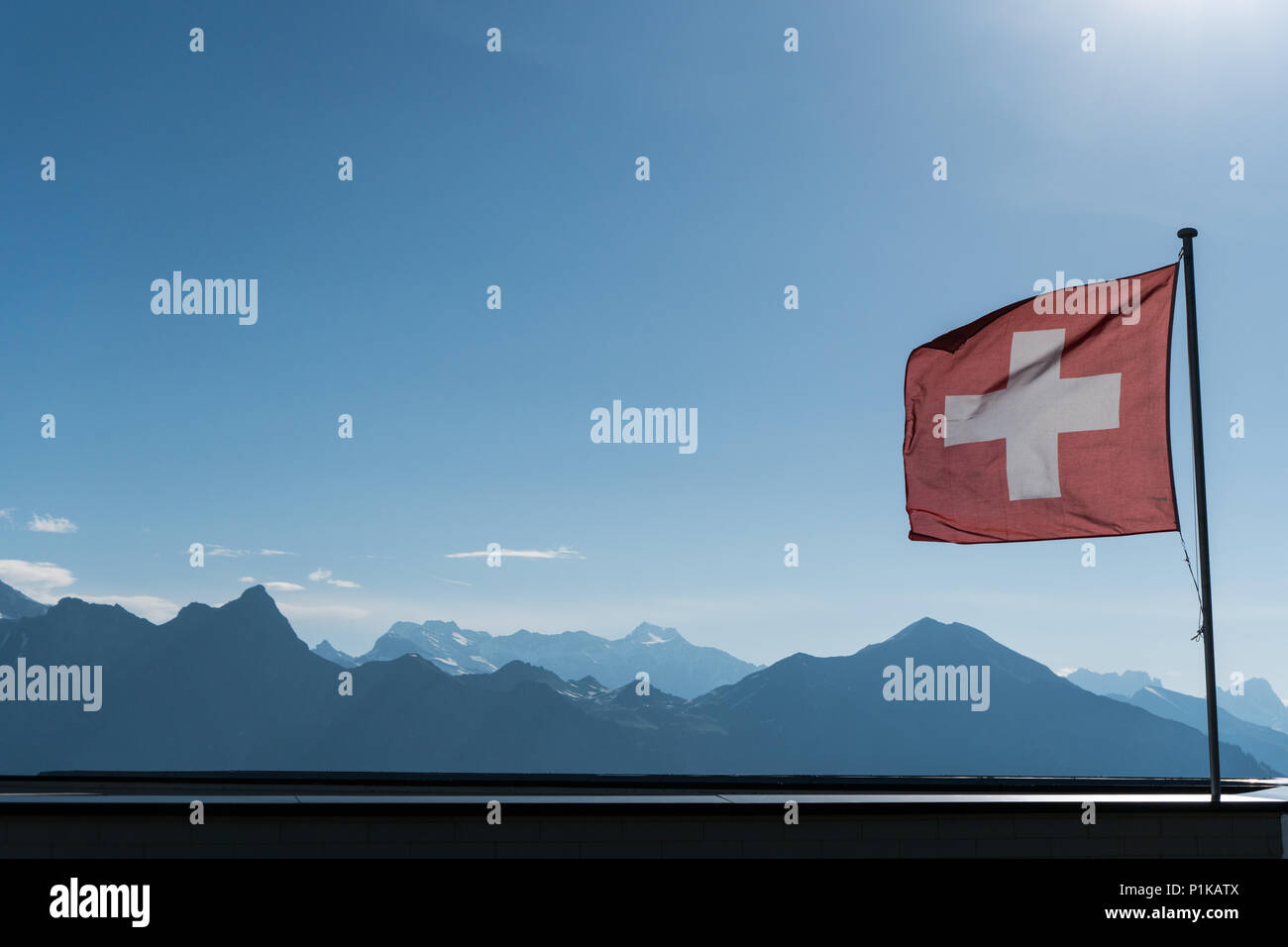 Swiss flag blowing in the wind with a gorgoues mountain landscape and blue sky behind Stock Photo