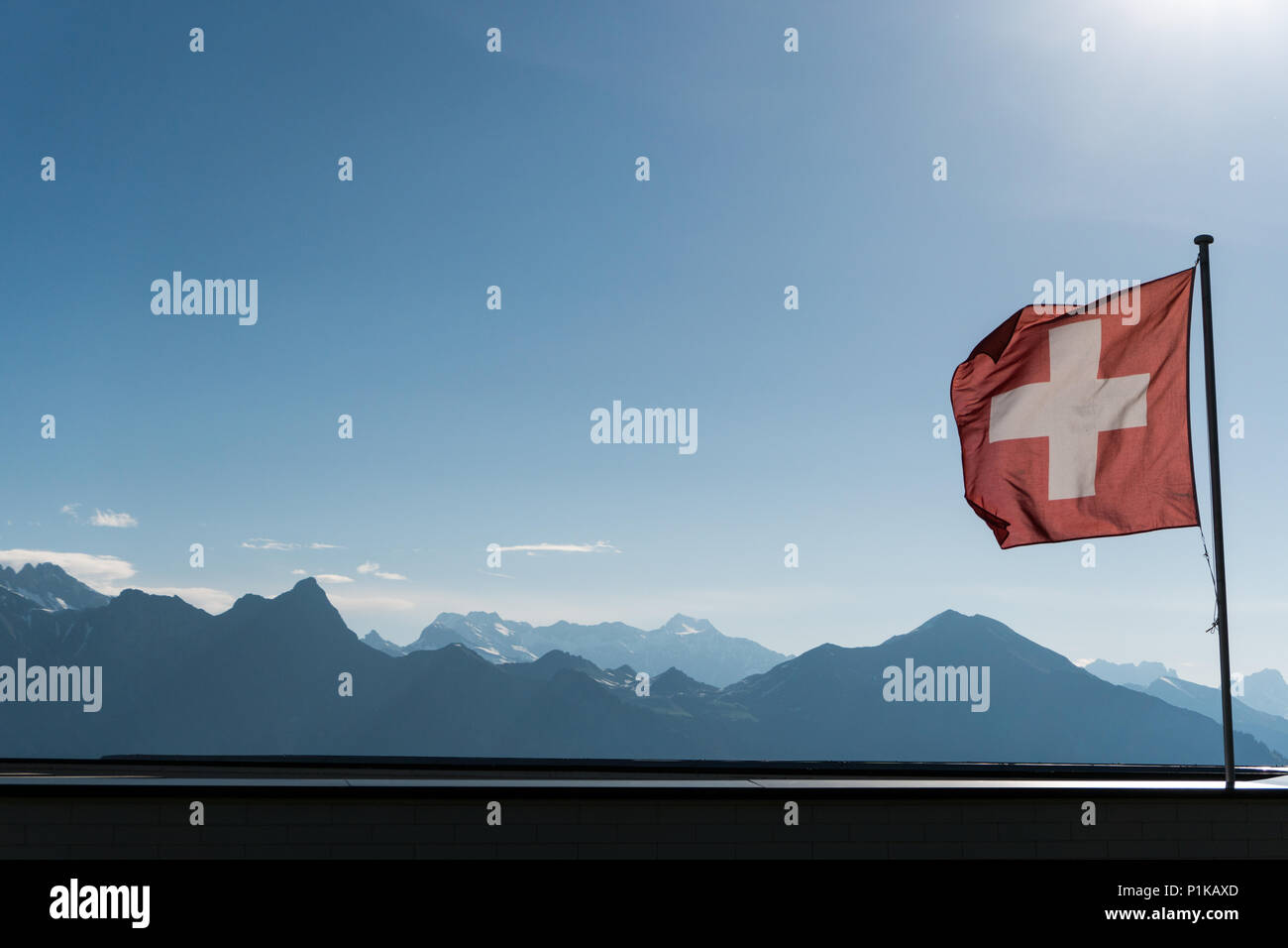 Swiss flag blowing in the wind with a gorgoues mountain landscape and blue sky behind Stock Photo