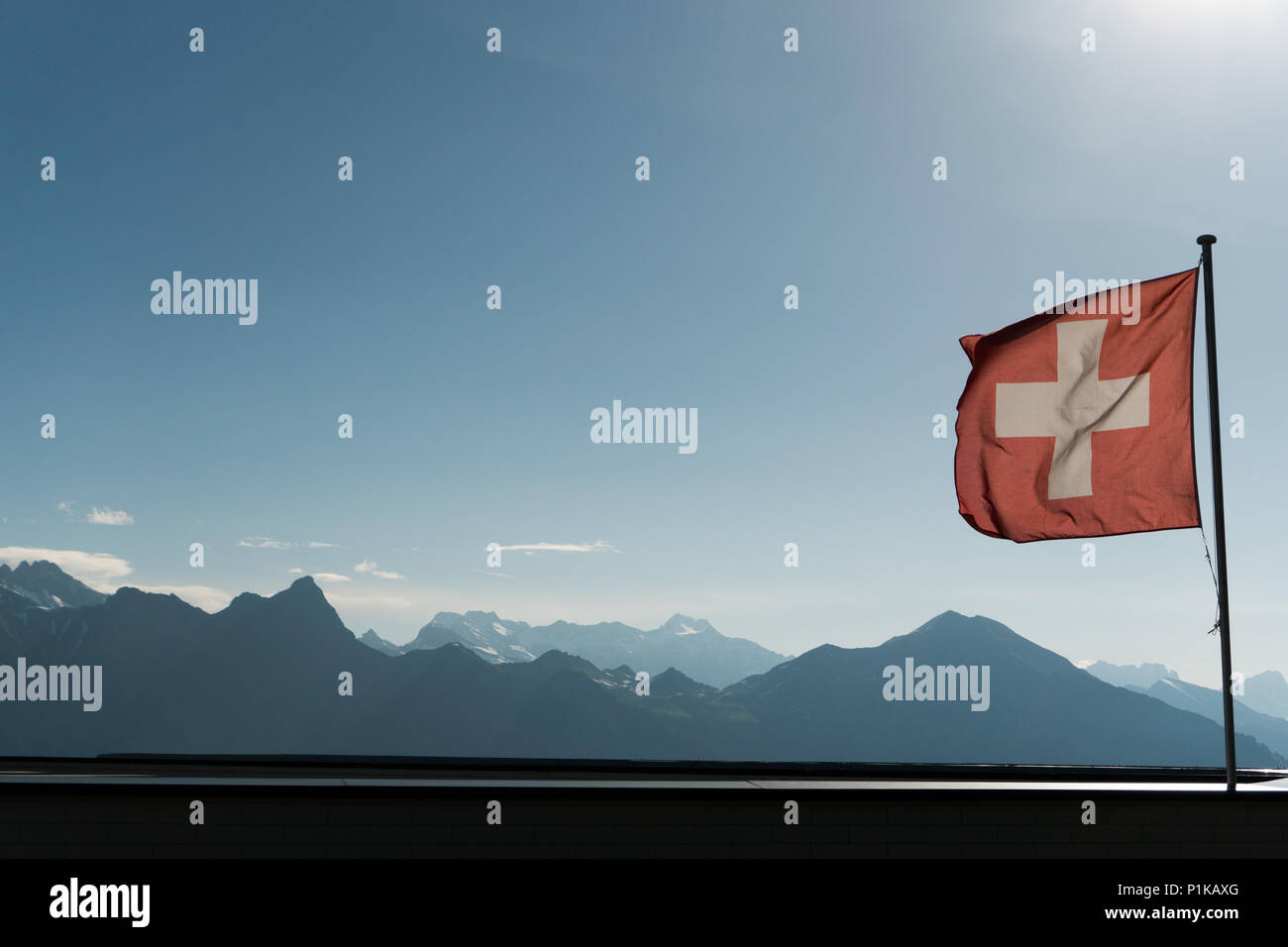 Swiss flag blowing in the wind with a gorgoues mountain landscape and blue sky behind Stock Photo