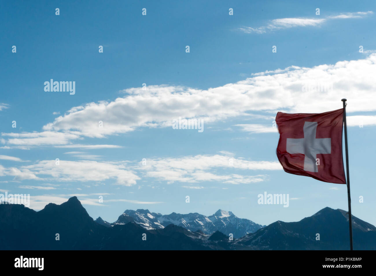 Swiss flag blowing in the wind with a gorgoues mountain landscape and blue sky behind Stock Photo