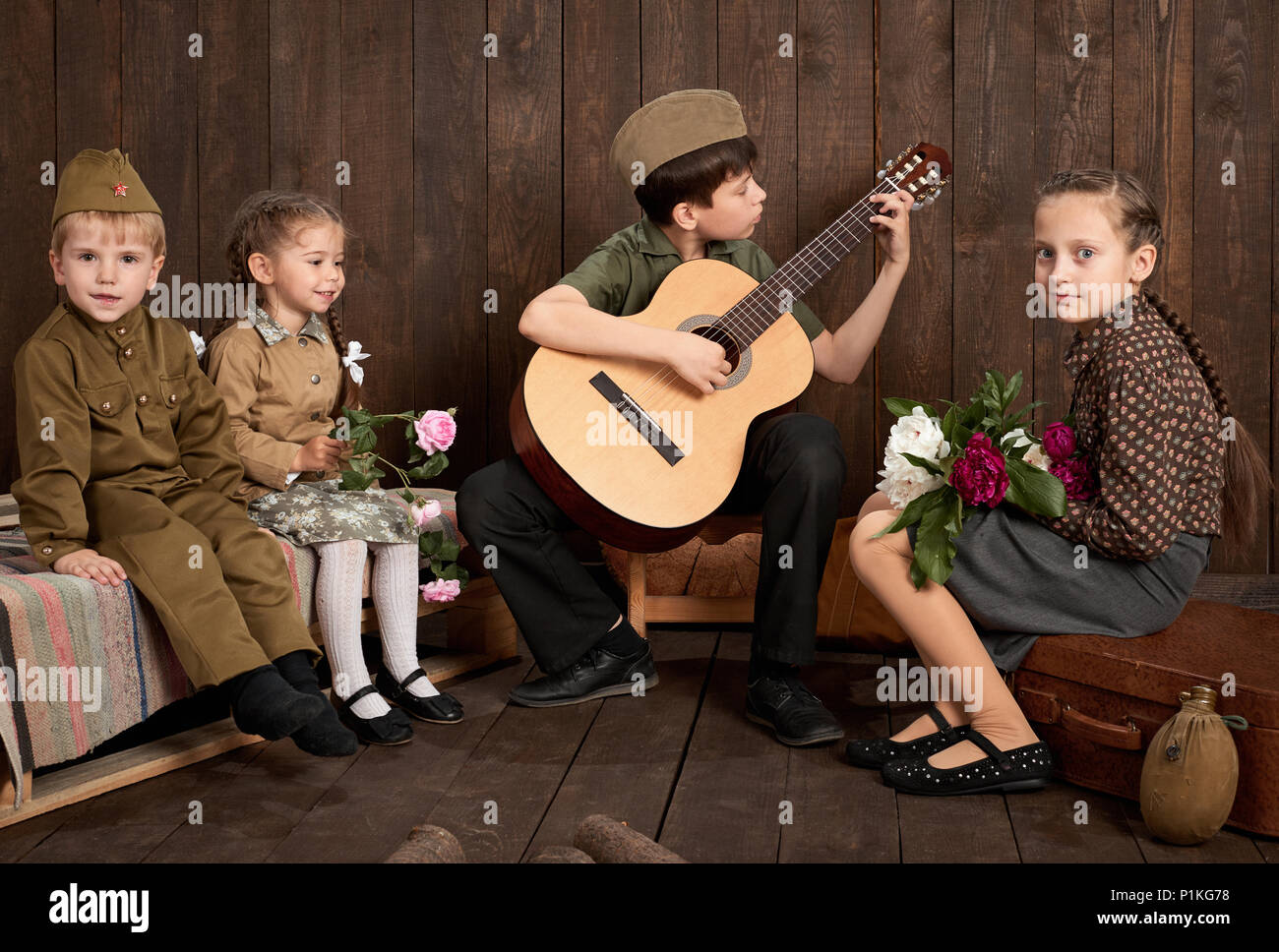 children are dressed in retro military uniforms sitting and playing guitar, sending a soldier to the army, dark wood background, retro style Stock Photo