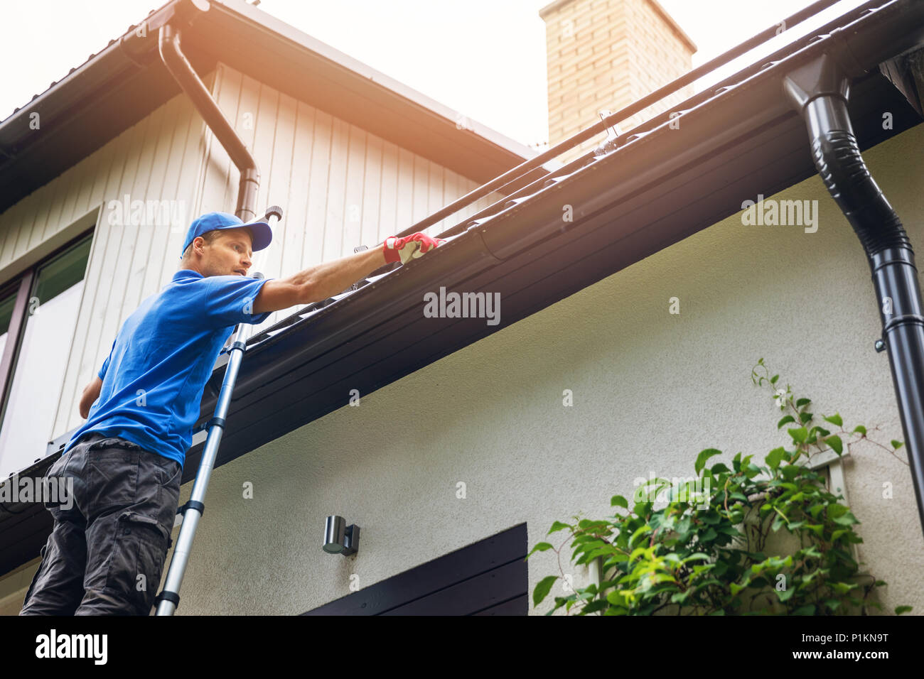 man on ladder cleaning house gutter from leaves and dirt Stock Photo