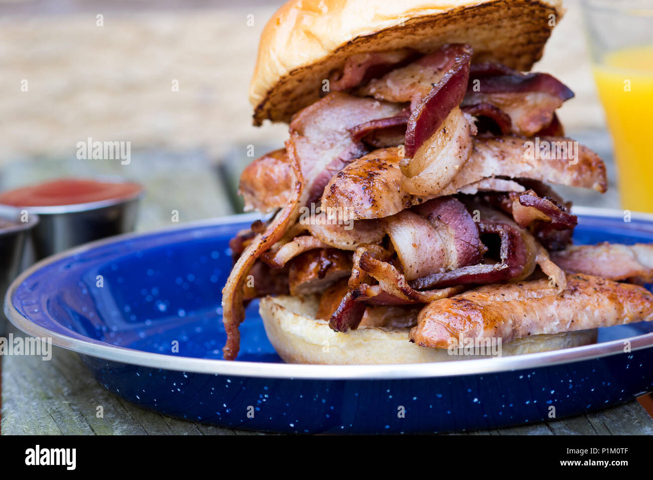 Sausage & Streaky Bacon in a brioche bun, with sauces and orange juice Stock Photo