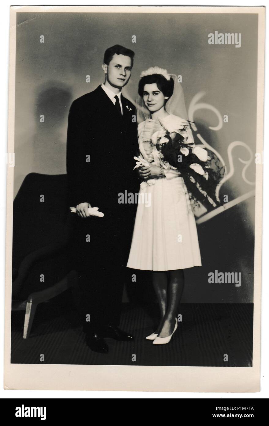 THE CZECHOSLOVAK SOCIALIST REPUBLIC - APRIL 4, 1964: Retro photo shows bride with white kala flowers and groom wears a dark suit and white gloves. Black & white vintage photography of wedding couple. Stock Photo