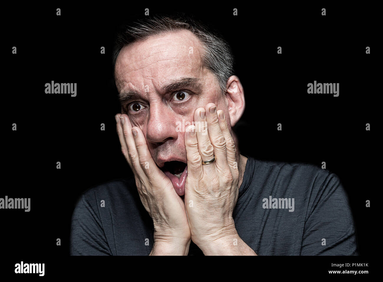 Closeup High Contrast Portrait of Shocked Horrified Man with Hands to Face on Black Background Stock Photo