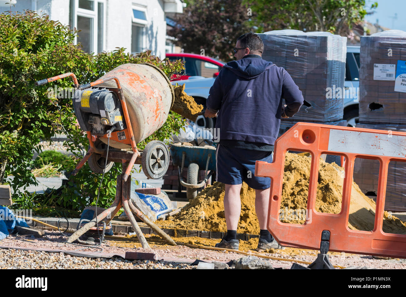 Man placing sand into a portable cement mixer as part of construction work on a residential property in the UK. Stock Photo