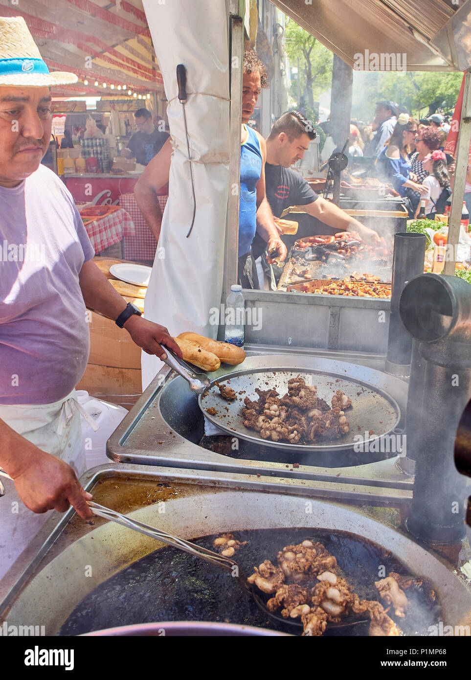 Hispanic cook frying Entresijos (Lamb Mesentery) in a stall of a Street Food fair. Others cookers cooking Sausages and Oreja de Cerdo (Pork Ear) Stock Photo