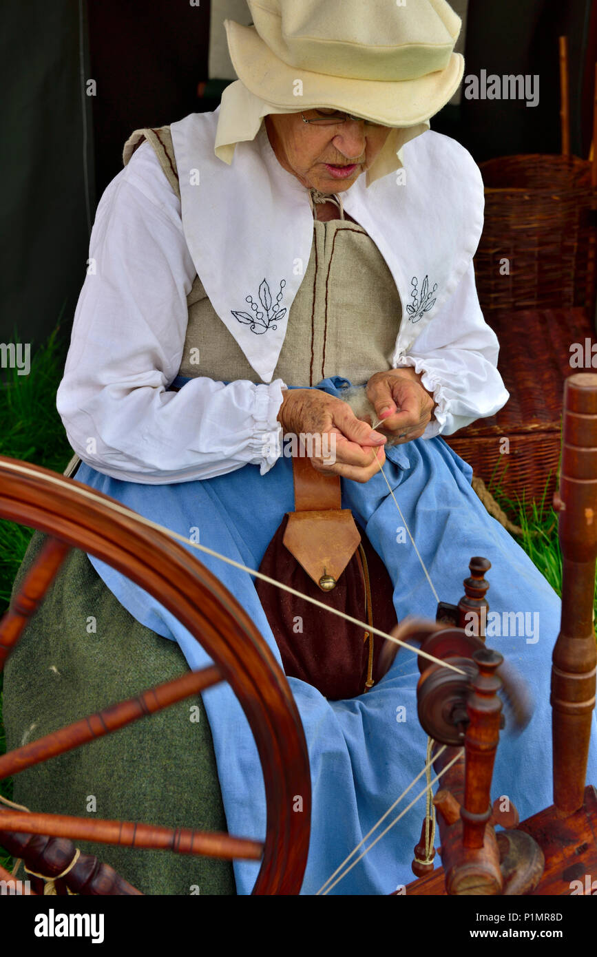 Woman in 17th century costume spinning natural wool thread with spinning wheel during English Civil War reenactment Stock Photo