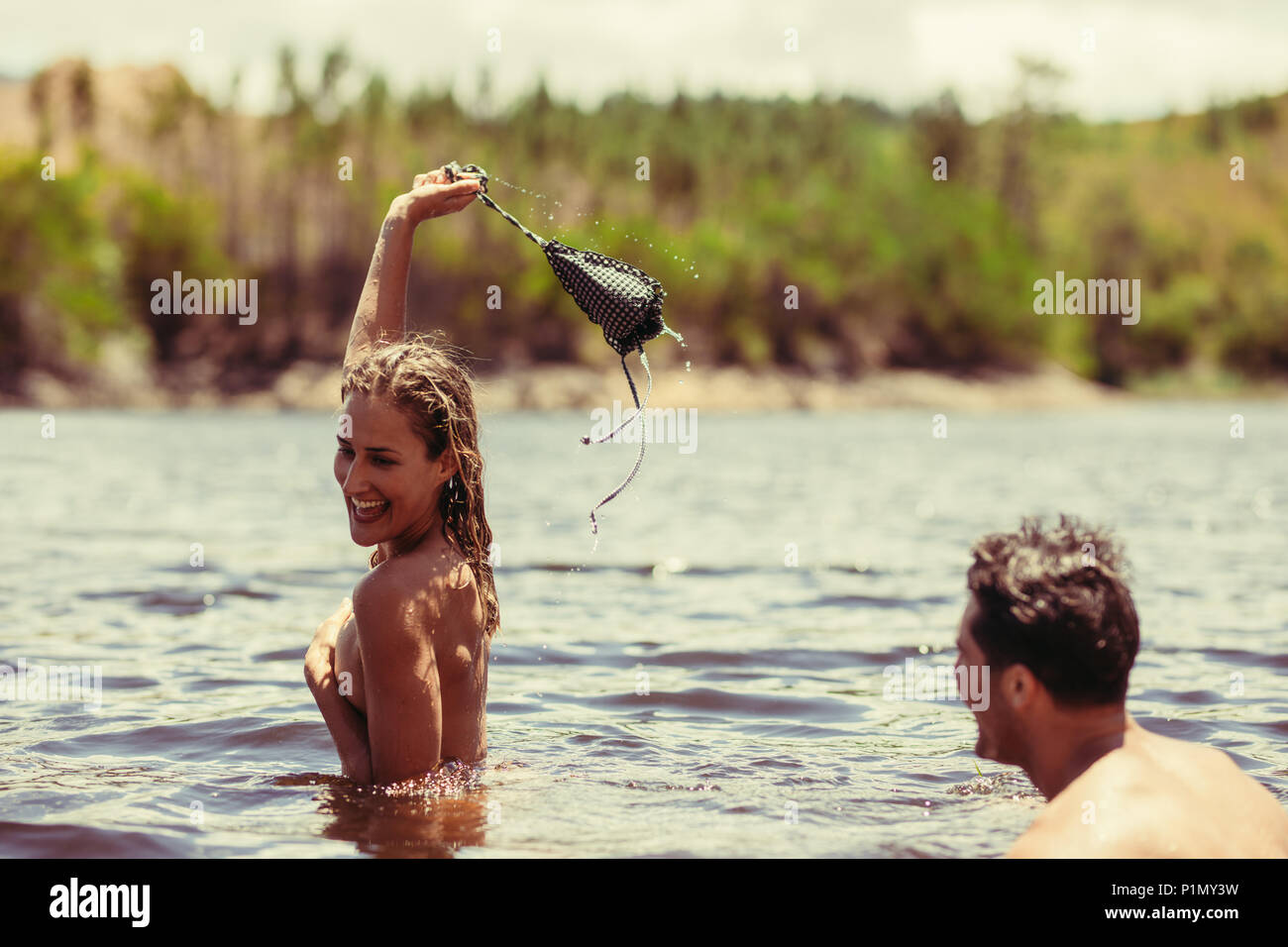 Pair of happy people enjoying bathing in lake during hot summer. Woman  removing her bra and smiling with her boyfriend Stock Photo - Alamy