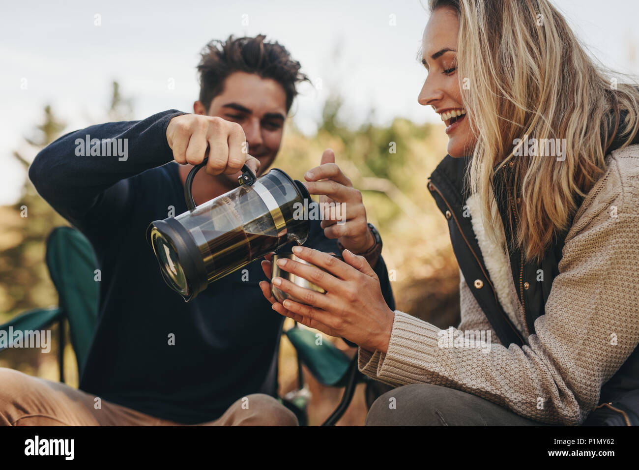 Young couple having coffee at a campsite. Man serving coffee to woman. Stock Photo