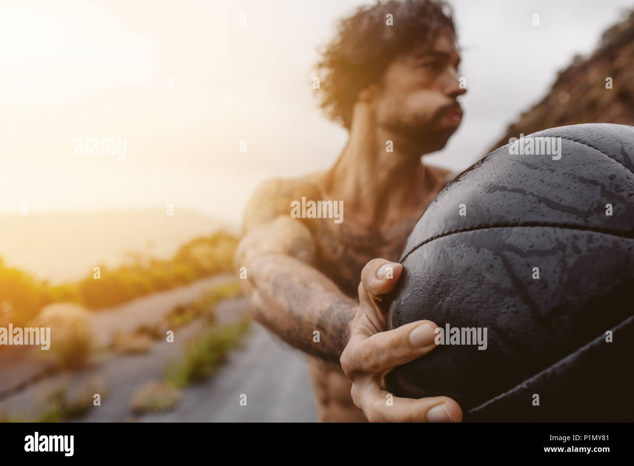 Hand of young man exercising with medicine ball outdoor. Sportsman exercising outdoors on a rainy day. Stock Photo