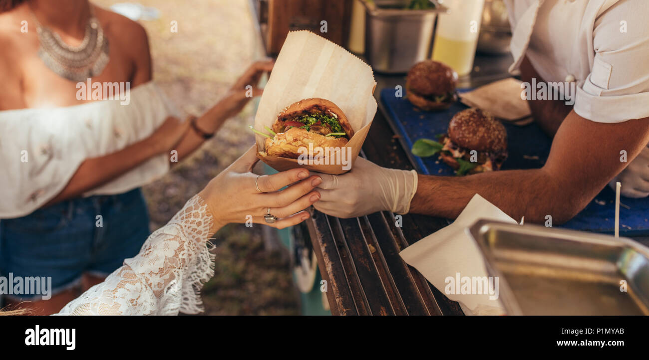 Woman hand reaching for a burger at food truck. Closeup of food truck salesman serving burger to female customer. Stock Photo