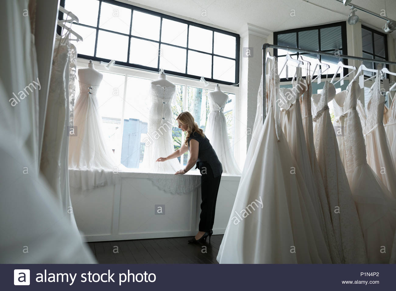 Bridal boutique owner arranging wedding dress window display Stock Photo