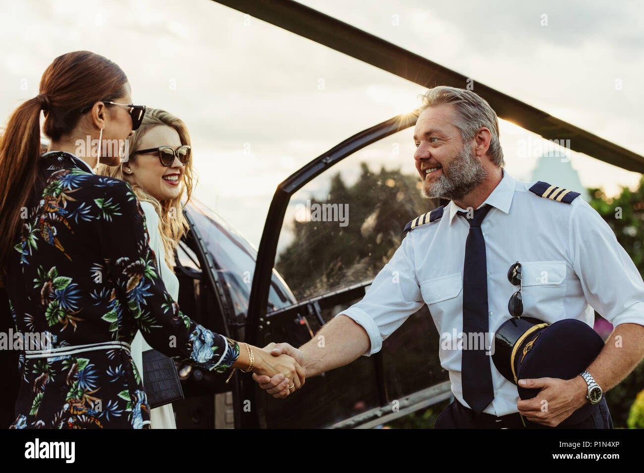 Helicopter pilot shaking hands with two women and smiling. Two women traveling by a private helicopter with pilot greeting them. Stock Photo