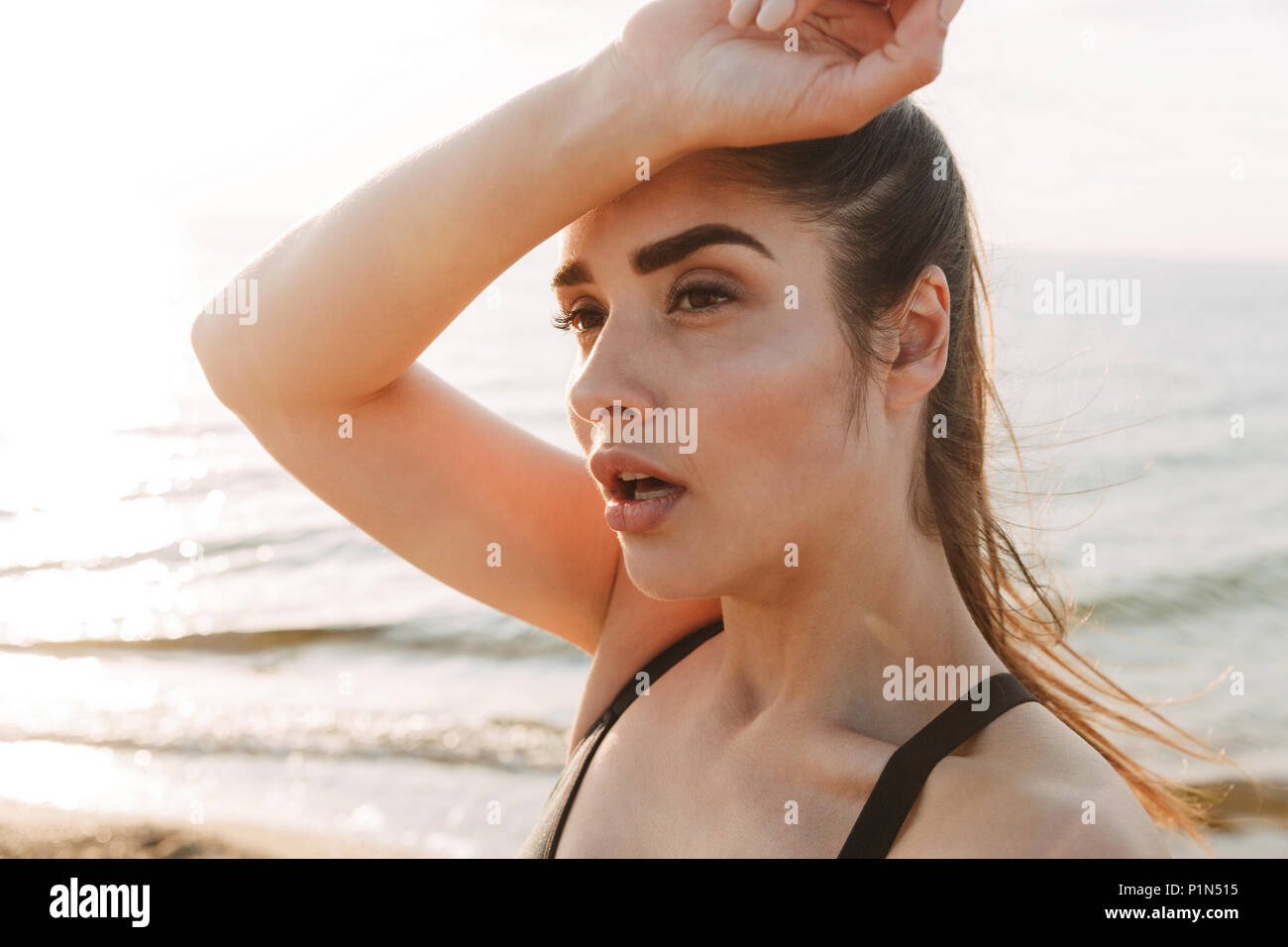 Close up portrait of a tired young sportswoman wiping forehead with her hand at the beach Stock Photo