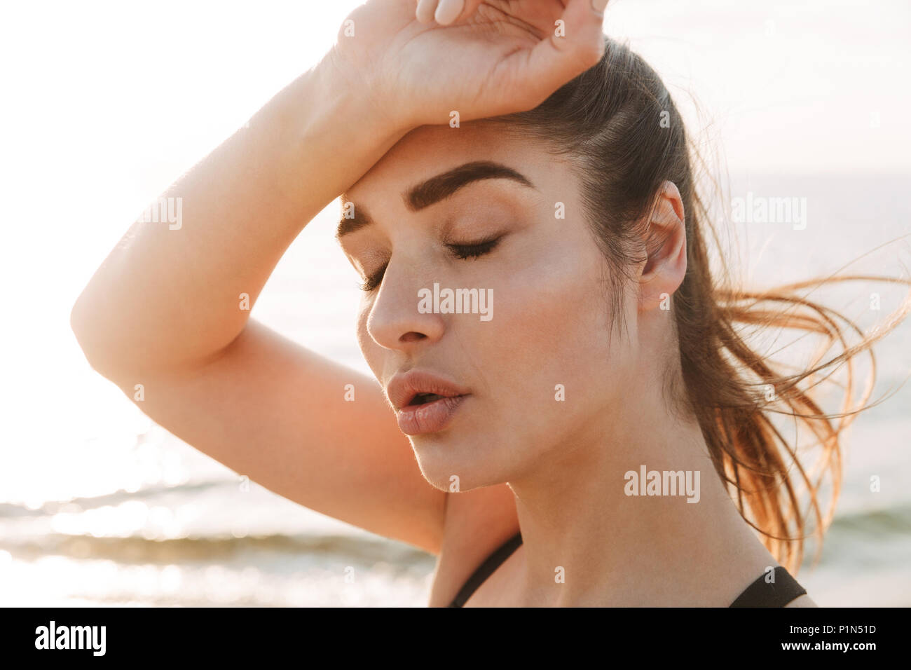 Close up portrait of an exhausted young sportswoman wiping forehead with her hand at the beach Stock Photo