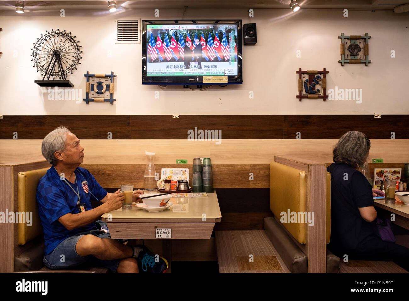 At a local restaurant in Hong Kong, a local watches a TV screen showing the historic moment when US President Donald Trump and North Korea leader Kim Jong-un meet for the first time during the Singapore peace-keeping and denuclearisation Summit. Stock Photo