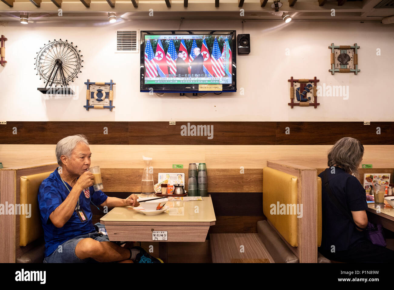At a local restaurant in Hong Kong, a local watches a TV screen showing the historic moment when US President Donald Trump and North Korea leader Kim Jong-un meet for the first time during the Singapore peace-keeping and denuclearisation Summit. Stock Photo