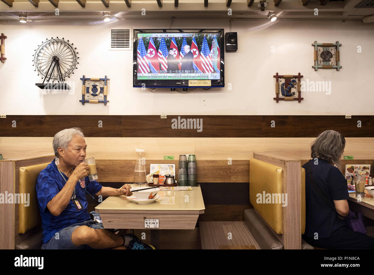 Kowloon, Hong Kong. 12th June, 2018. At a local restaurant in Hong Kong, a local watches a TV screen showing the historic moment when US President Donald Trump and North Korea leader Kim Jong-un meet for the first time during the Singapore peace-keeping and denuclearisation Summit. Credit: Miguel Candela/SOPA Images/ZUMA Wire/Alamy Live News Stock Photo